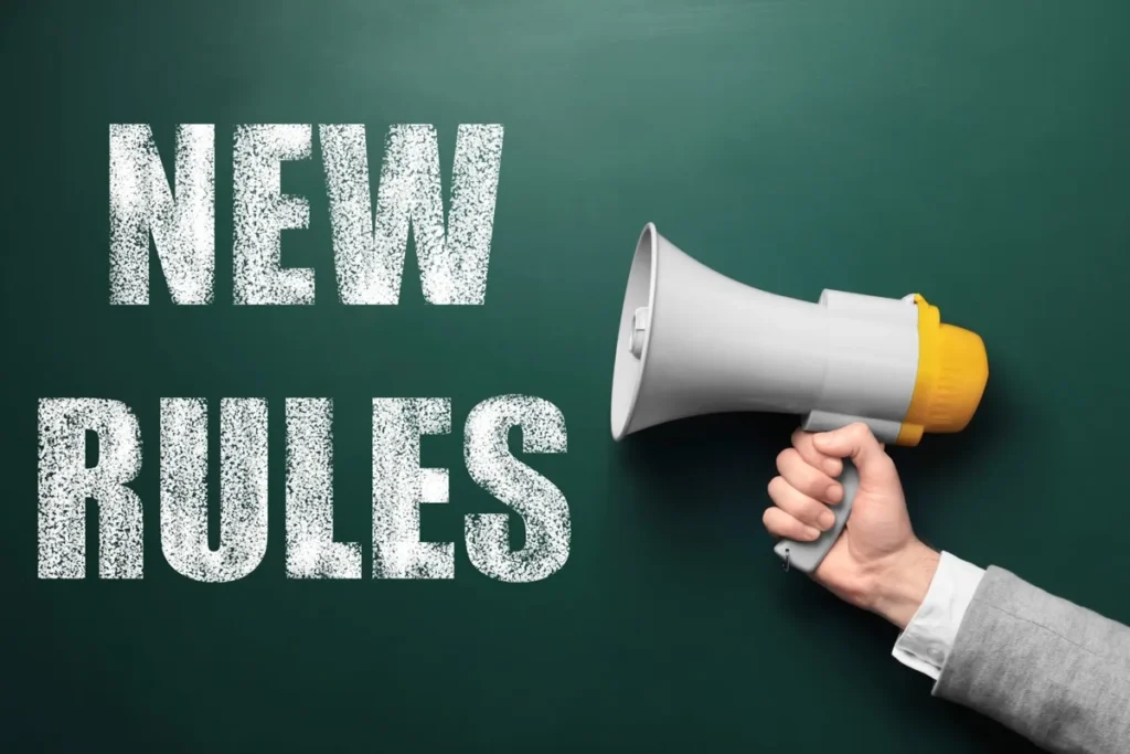 NEW RULES written in chalk on a green chalkboard next to a hand holding a megaphone