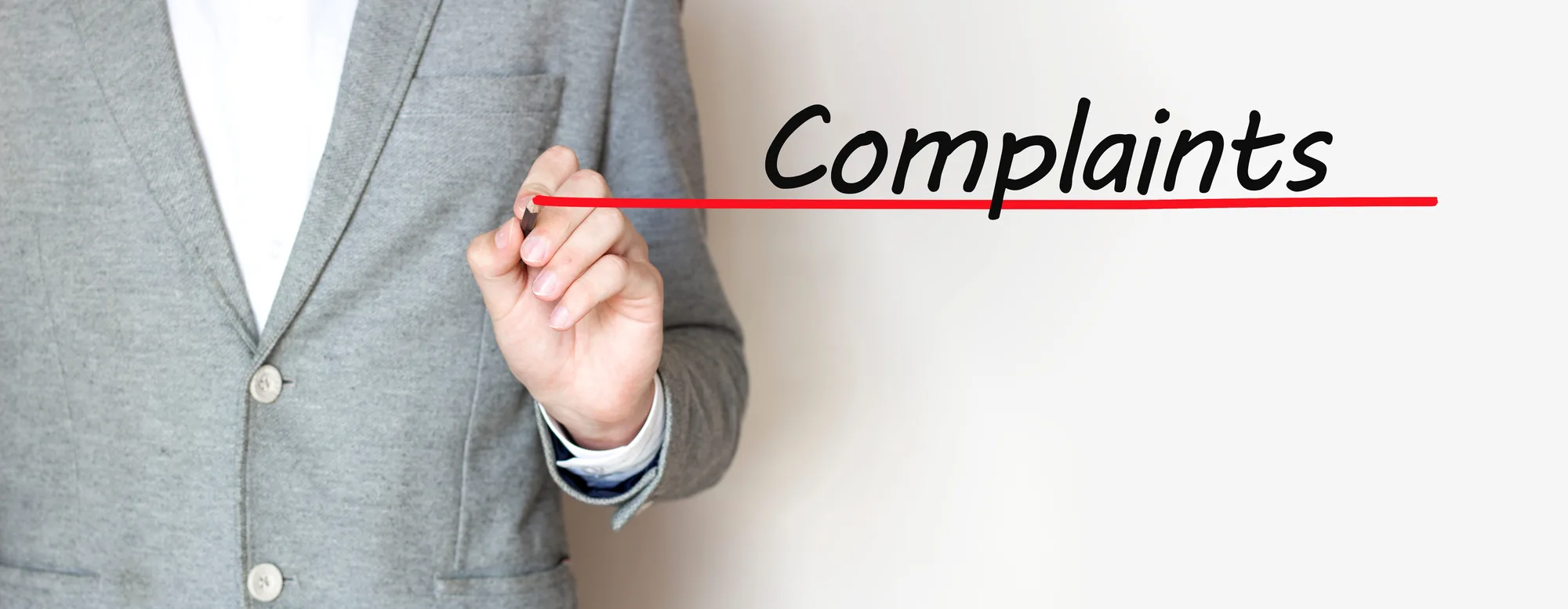 A hand writing the word Complaints in black marker with a red underline