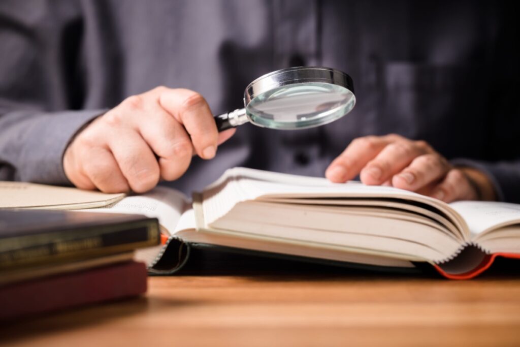 Closeup of a man using a magnifying glass over books, searching for information